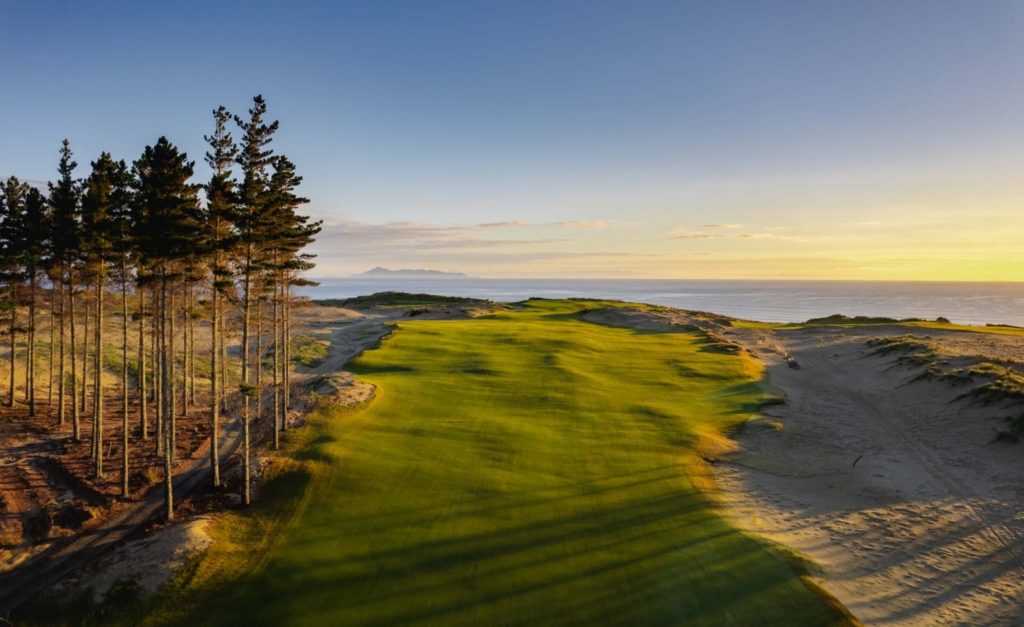 Heletranz helicopter flying over dramatic coastal cliffs, approaching Te Arai Links for a luxury heli golf experience.